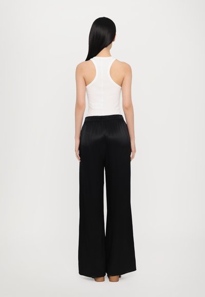 Débardeur blanc sans manches avec un design dos nageur, associé à un pantalon noir ample à jambe large. Tissu doux et texture lisse avec une taille élastique.