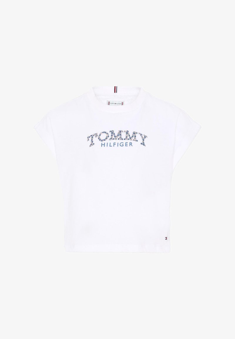 Witte cropped T-shirt met bloemrijke "TOMMY" tekst en blauwe "HILFIGER" logo eronder op de borst, korte vleugelvormige mouwen en een ronde hals.