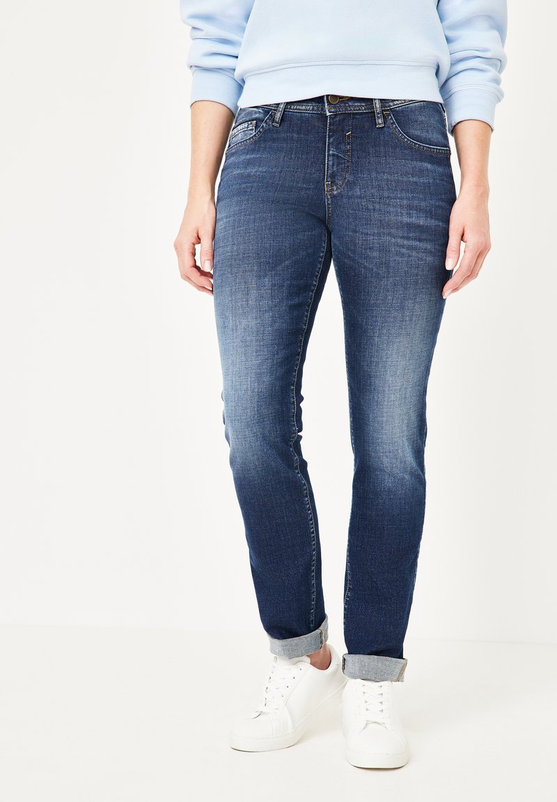 Dunkelblaue Jeans mit leichtem Verblassen, mit mittlerer Leibhöhe, Fünf-Taschen-Design und umgeschlagenen Säumen, getragen mit weißen Sneakers.