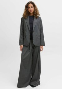 Sivi karo s pikčastim vzorcem z režastimi reverji in dvema sprednjima žepoma, kombiniran z širokimi hlačami v enakem tkanju. Tekstura s subtilnimi črtami.