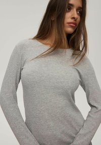 Szara, prążkowana bluzka z długim rękawem i szerokim dekoltem. Miękka tekstura i dopasowany krój, z delikatnymi wariacjami w wzorze materiału.