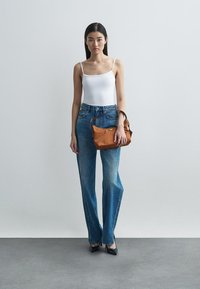 White fitted tank top, high-waisted blue jeans with side stitching details, brown leather bag, black pointed heels, minimalistic background.