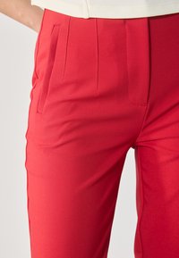 Pantalons ajustés rouges en tissu lisse et extensible, dotés de poches latérales et de plis avant subtils pour un look structuré.
