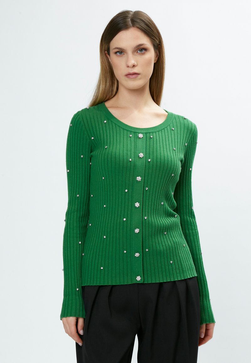 Cardigan verde a coste con maniche lunghe, scollatura a girocollo, chiusura frontale con bottoni e impreziosito da accenti floreali argentati su tutta la superficie.