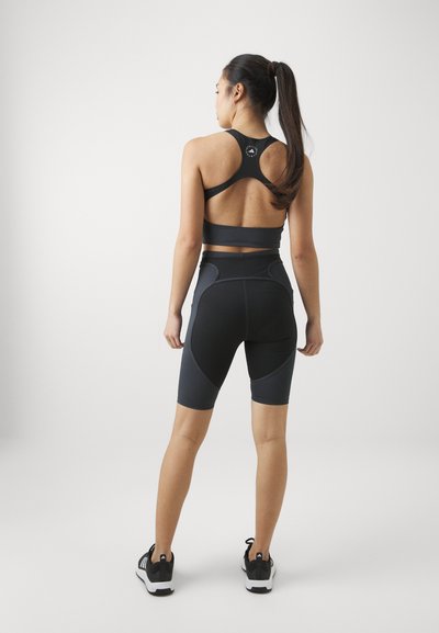 Black sports bra and high-waisted shorts with contrasting panels, fitted design, smooth texture, and athletic shoes with white soles.