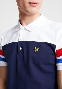 Navy blue polo shirt with white collar, featuring red and blue striped sleeves. Includes yellow embroidered logo on the chest.