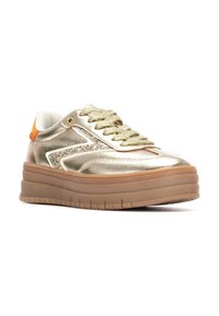 Zapatilla dorada metálica con una parte superior texturizada, acentos de purpurina y una suela gruesa beige. Presenta cordones verdes y una lengüeta en el talón de color naranja.