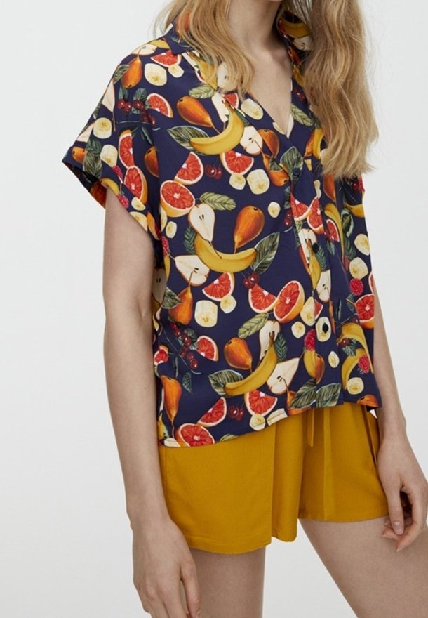 Short-sleeve, navy top with vibrant fruit pattern including bananas, pears, and citrus. Paired with solid yellow shorts. Smooth fabric.