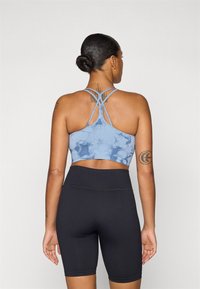 Top desportivo azul com padrão tie-dye, com alças cruzadas nas costas, combinado com calções altos pretos com riscas. Tecido suave e design ajustado.