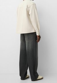 Giacca in pile crema con una vestibilità comoda e maniche lunghe, abbinata a jeans a gamba larga scuri e sneakers chiare.