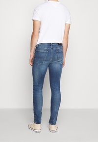 Modré slim-fit džíny s vybledlým vzhledem, pěti kapsami a koženou nášivkou. Nosit s bílým tričkem a béžovými teniskami.