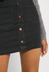 Svart denimkjol med knäppning framtill, två framfickor och en figurnära silhuett. Kopparfärgade knappar ger kontrast mot tyget.