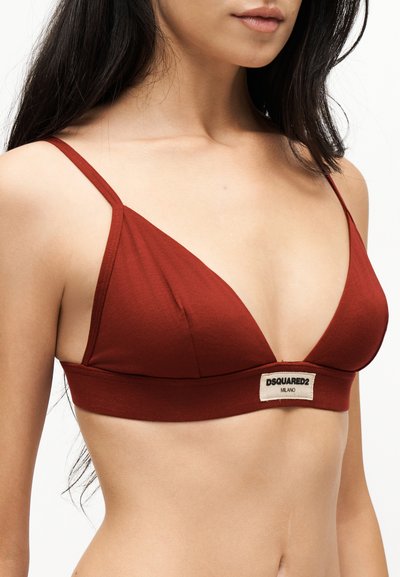 Γυναίκα που φοράει ένα τριγωνικό bralette σε σκουριά κόκκινο με λεπτές τιράντες και μια μικρή ορθογώνια ετικέτα DSQUARED2 Milano στο μπροστινό τμήμα.