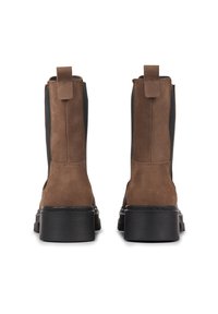 Brown suede ankle boots with elastic side panels, pull tabs, and thick black rubber soles, featuring a smooth texture and modern design.