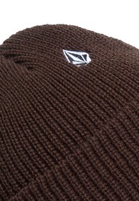 Brown knitted beanie hat with ribbed texture; features a small white and black logo patch. Durable material, snug fit.