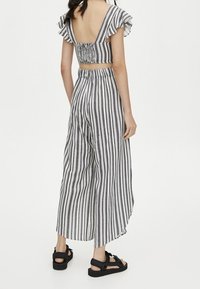 Gestreepte twee-delige outfit met een cropped top met ruches aan de mouwen en wijde broek. Gemaakt van lichtgewicht stof in grijs en wit.