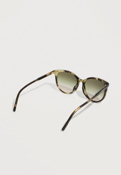 Γυαλιά ηλίου με σχέδιο χελώνας και στρογγυλούς φακούς σε βαθμιαία απόχρωση του πράσινου, ανοιχτά να στηρίζονται σε λευκή επιφάνεια.