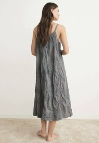 Abito grigio senza maniche realizzato in tessuto texturizzato con ricami floreali. La forma fluida si estende sotto il ginocchio, progettato per comfort e facilità.