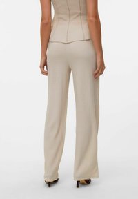Pantaloni beige testurizzati con una vestibilità ampia, caratterizzati da una forma leggermente svasata. Il design include una cintura liscia e sottili righe verticali.