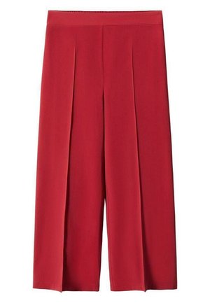 Persona vistiendo un suéter beige acanalado con cremallera frontal y mangas largas, combinado con pantalones rojos de talle alto, con los brazos cruzados.