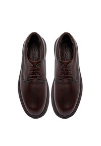 Zapatos derby de cuero marrón con un acabado texturizado, punta redondeada y cordones en la parte frontal, con una suela lisa y un diseño minimalista.