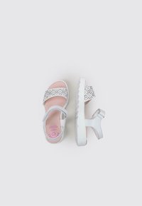 Sandalias blancas con una correa estampada, suela texturizada y correa de tobillo ajustable. Plantilla de color rosa suave con el logo de la marca. Diseño ligero.