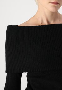 Schwarzer schulterfreier Pullover mit gerippter Textur und taillierter Passform, ausgestattet mit breiten Rippen am Halsausschnitt und langen Ärmeln.