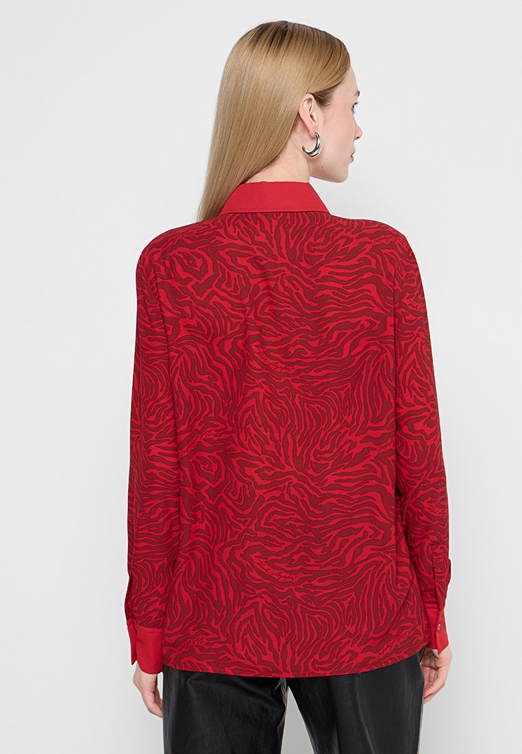 Chemise rouge avec un motif texturé en zèbre, à manches longues et col. Dispose de poignets à boutons et d'une coupe légèrement ample.