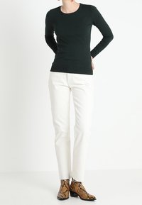 Ciemnozielona bluzka z długim rękawem zestawiona z białymi dżinsami, uzupełniona brązowymi botkami z nadrukiem wężowej skóry i spiczastym noskiem.