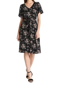 Vestido negro con estampado floral en rosa y blanco, mangas cortas, escote en V, cintura ajustada con un lazo, falda fluida, usado con sandalias negras.