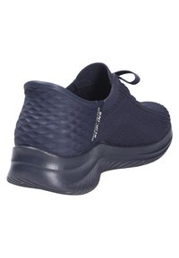 Zapatilla deportiva azul marino con parte superior de malla texturizada, cierre de cordones y suela acolchada. Presenta un talón liso y la marca "Skechers Skrunch".