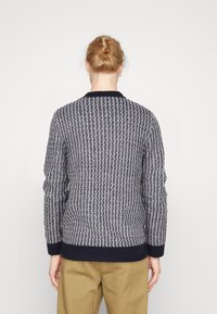 Laivastonsininen ja vaaleanharmaa teksturoitu neule, jossa on ribbineuloskaulus, aaltoileva kuvio ja istuva vyötärönauha. Yhdistetty beigeihin housuihin.