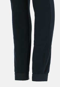 Sorte fleecebukser med en glat tekstur, der har elastiske manchetter ved anklerne og lige ben. Stoffet virker blødt og varmt.