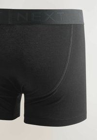 Fekete boxer alsónadrág, puha anyagból, sima textúrával, márkázott, rugalmas derékpánttal és letisztult dizájnnal.