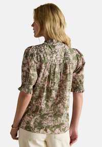 Lillelilleline blouse rohelises ja roosas, puffse varrukatega, volanud mansettidega ja pleated seljaga. Valmistatud kergest kangast, millel on tekstureeritud muster.