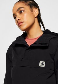 Giacca a pullover nera realizzata in tessuto leggero e resistente all'acqua. Presenta una tasca frontale, cappuccio e una toppa con il marchio sul petto.