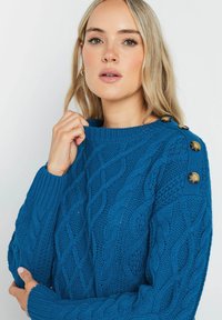 Kabelstrickpullover in leuchtendem Blau, mit gerippten Bündchen und rundem Halsausschnitt, verziert mit goldfarbenen Knöpfen an der Schulter.