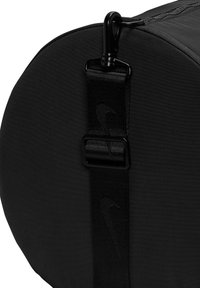 Svart sylinderformet bag laget av teksturert stoff, med en solid stropp og en metallklemme. Minimalistisk design med subtile merkevare detaljer.