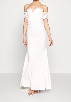 Biała sukienka z opuszczanymi ramionami, z głębokim dekoltem, koronkowymi zdobieniami na górze i dopasowaną, płynną sylwetką. Wykonana z gładkiej tkaniny.