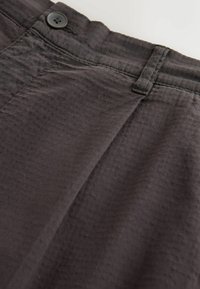 Dunkelgraue, strukturierte Stoffhose mit knöpfbarem Bund und Gürtelschlaufen-Detail, Nahaufnahme vor hellem Hintergrund.