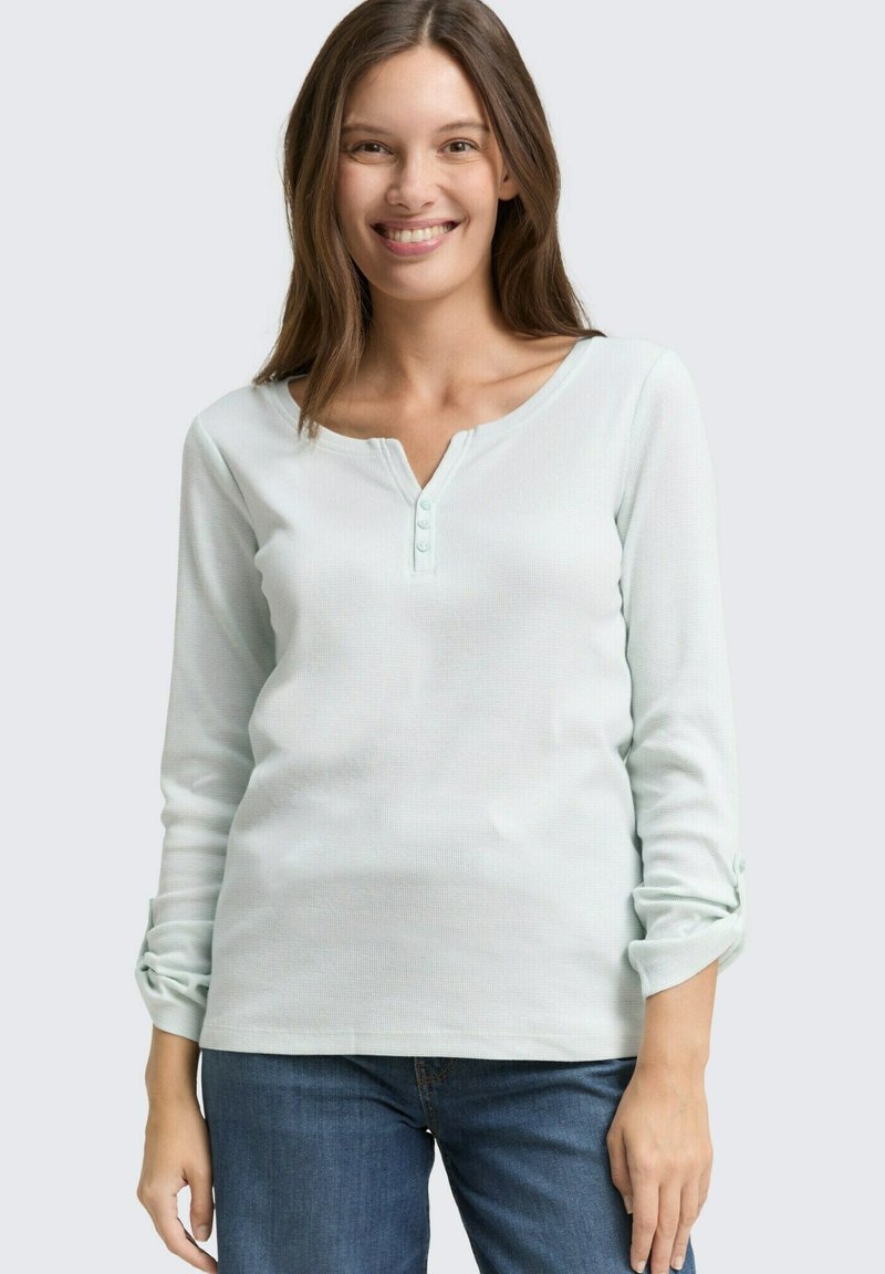 Top vert menthe à manches longues avec un col en V et une patte de boutonnage à trois boutons. Le tissu présente un tissage texturé. Le style comprend des poignets retroussés.