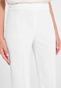 Pantaloni bianchi su misura realizzati in tessuto morbido, con vita alta, design dritto e cuciture laterali sottili senza tasche.