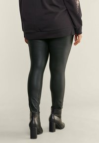 Zwarte neplederen leggings met een gladde textuur, gecombineerd met een zwarte sweatshirt met een subtiel ontwerp op de mouw. Gemaakt met blokhaklaarzen.