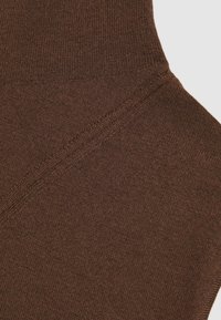 Hnedá pletená tkanina s hladkou štruktúrou, s diagonálnym švitom. Materiál sa zdá byť elastický a jemný.