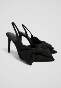 Zwarte hoge hak slingback schoenen van stof, met een spitse neus en een opvallende strikdetail aan de voorkant. Dunne stiletto hak.