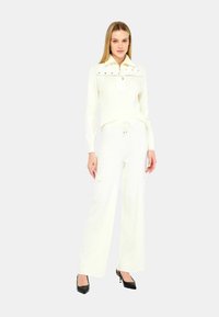 Set coordinato bianco composto da un top in maglia a costine con zip e colletto, e pantaloni a gamba larga con tasche cargo, abbinato a tacchi neri.