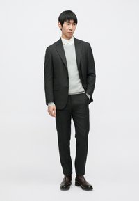 Costum gri cu dungi subtiri, croială strâmtă, purtat peste un pulover gri deschis, asortat cu ghete de piele maro închis până la gleznă. Design simplu, modern.