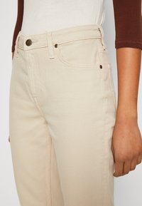 Světlé béžové džíny s vysokým pasem, s měděnými prvky, pěti kapsami a jemnými detaily šití.