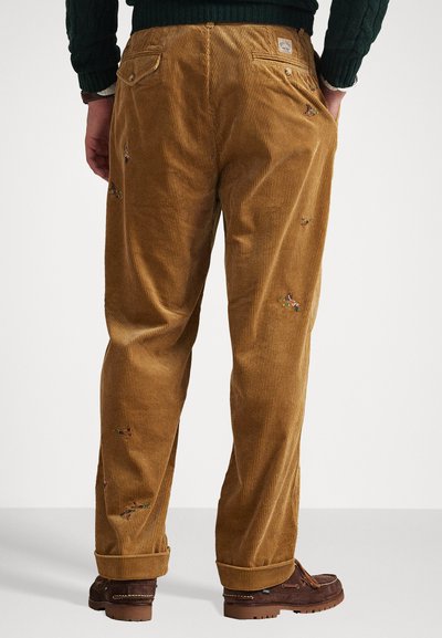 Bruine corduroy broeken met verticale ribbelstructuur, voorzien van subtiele borduursels, achterzakken en een opgerolde zoom.