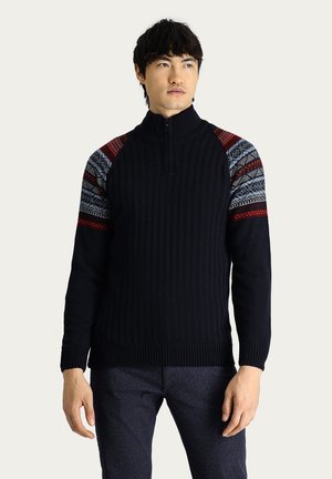 Suéter de canalé azul marino con alto cuello y cierre de cremallera, que presenta detalles de punto estampado en rojo y azul en los hombros.